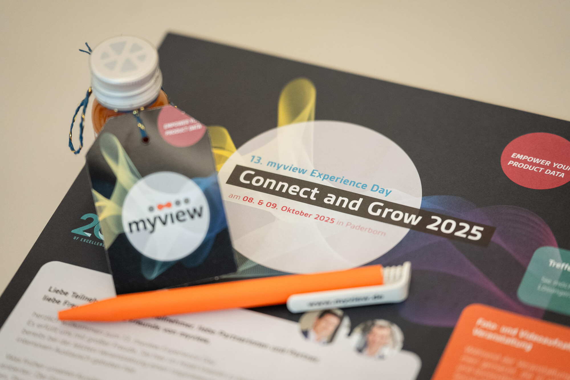 Teilnehmerausweis, Kugelschreiber und Getränk auf dem Event-Flyer zum myview Experience Day 2025 in Paderborn.