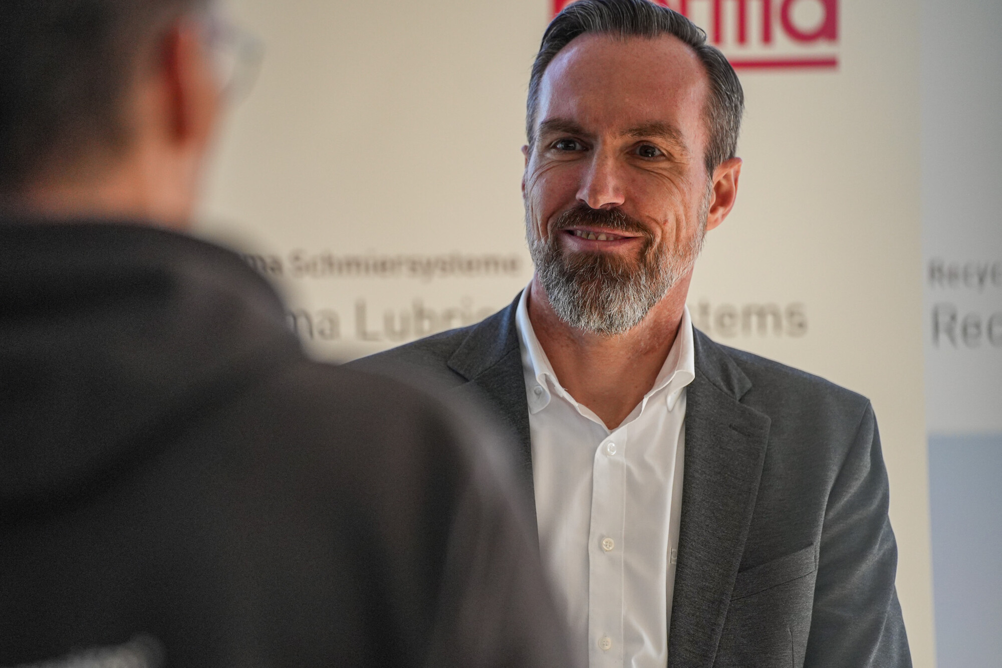 Geschäftsmann mit grauem Sakko im Gespräch, freundlicher Gesichtsausdruck, professionelle Business-Situation