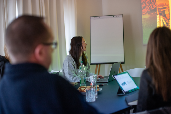 Mehrere Personen bei einer Besprechung im modernen Konferenzraum mit Laptop, Tablet und Flipchart.