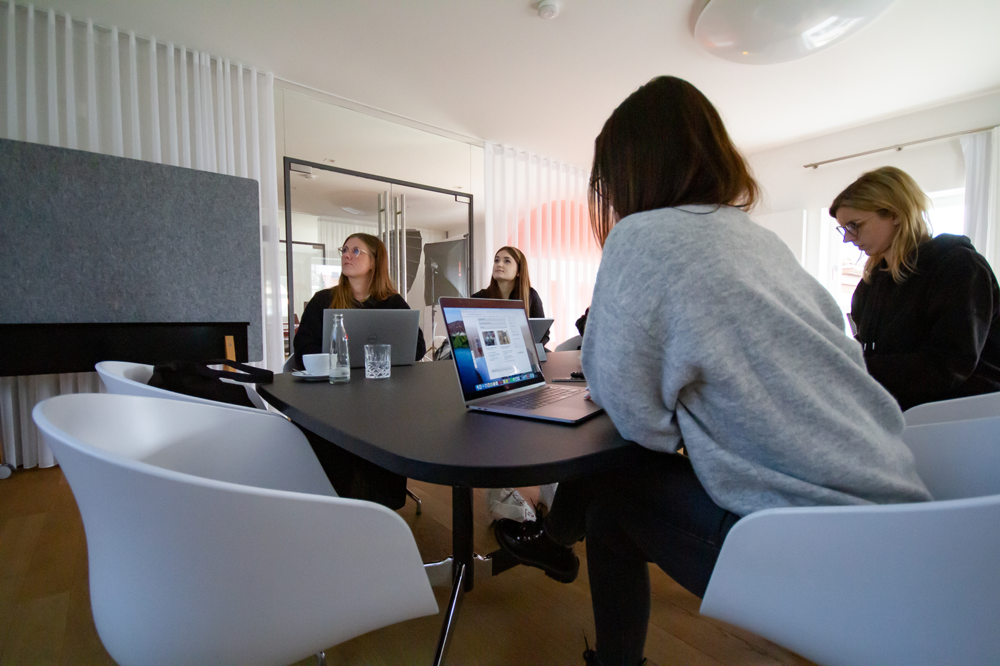 Vier junge Frauen arbeiten konzentriert mit Laptops an einem Besprechungstisch in modernem Büro.