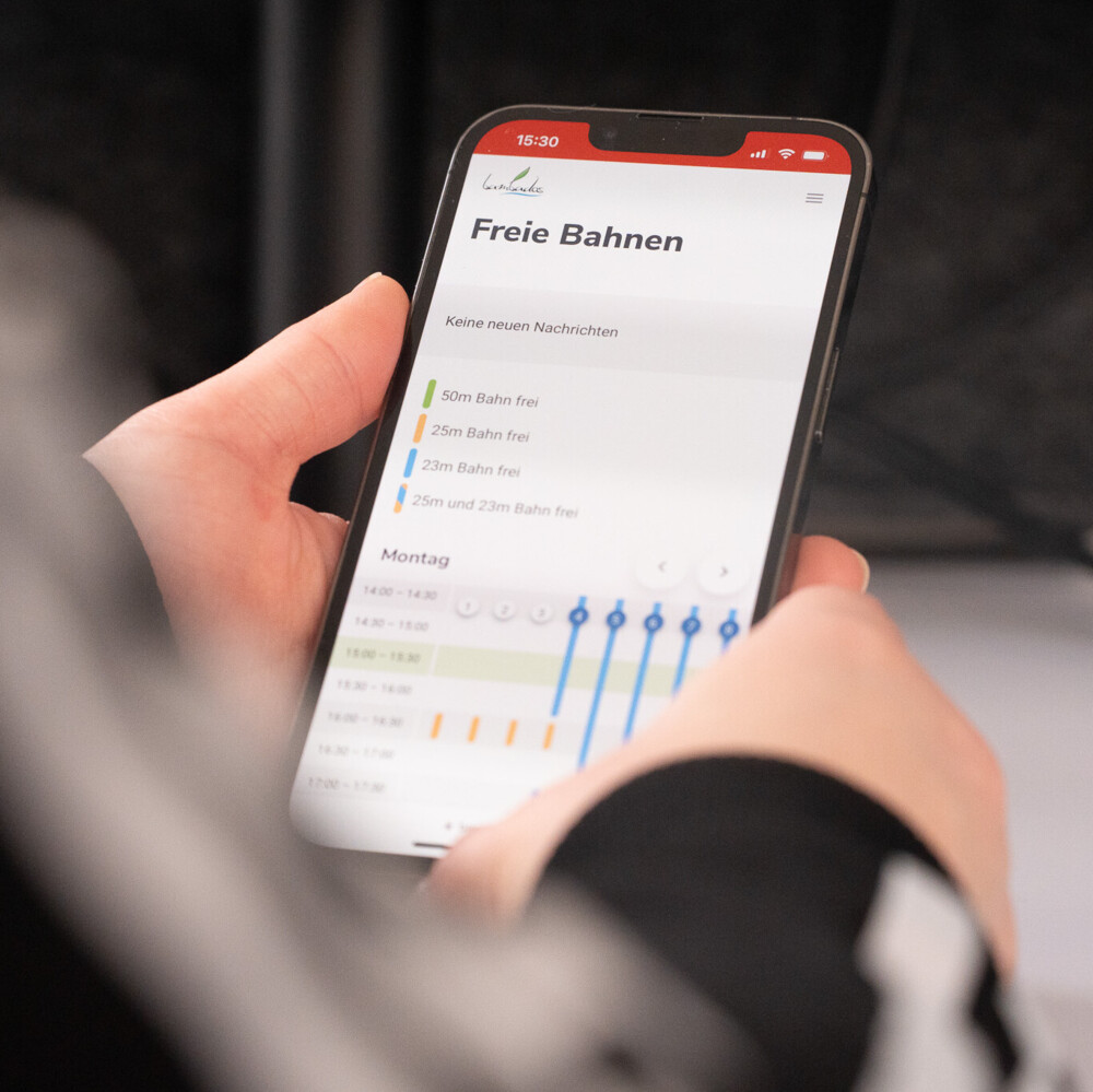 Person prüft Verfügbarkeit freier Bahnen in Schwimmbad-App auf Smartphone, zeigt verschiedene Zeiten und Bahnarten.