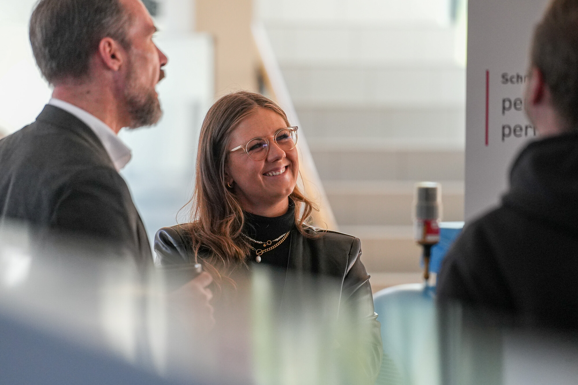 Professionelle Gesprächsrunde mit lächelnder Frau und Kollegen in modernem Büroambiente, Teamwork und Kommunikation.