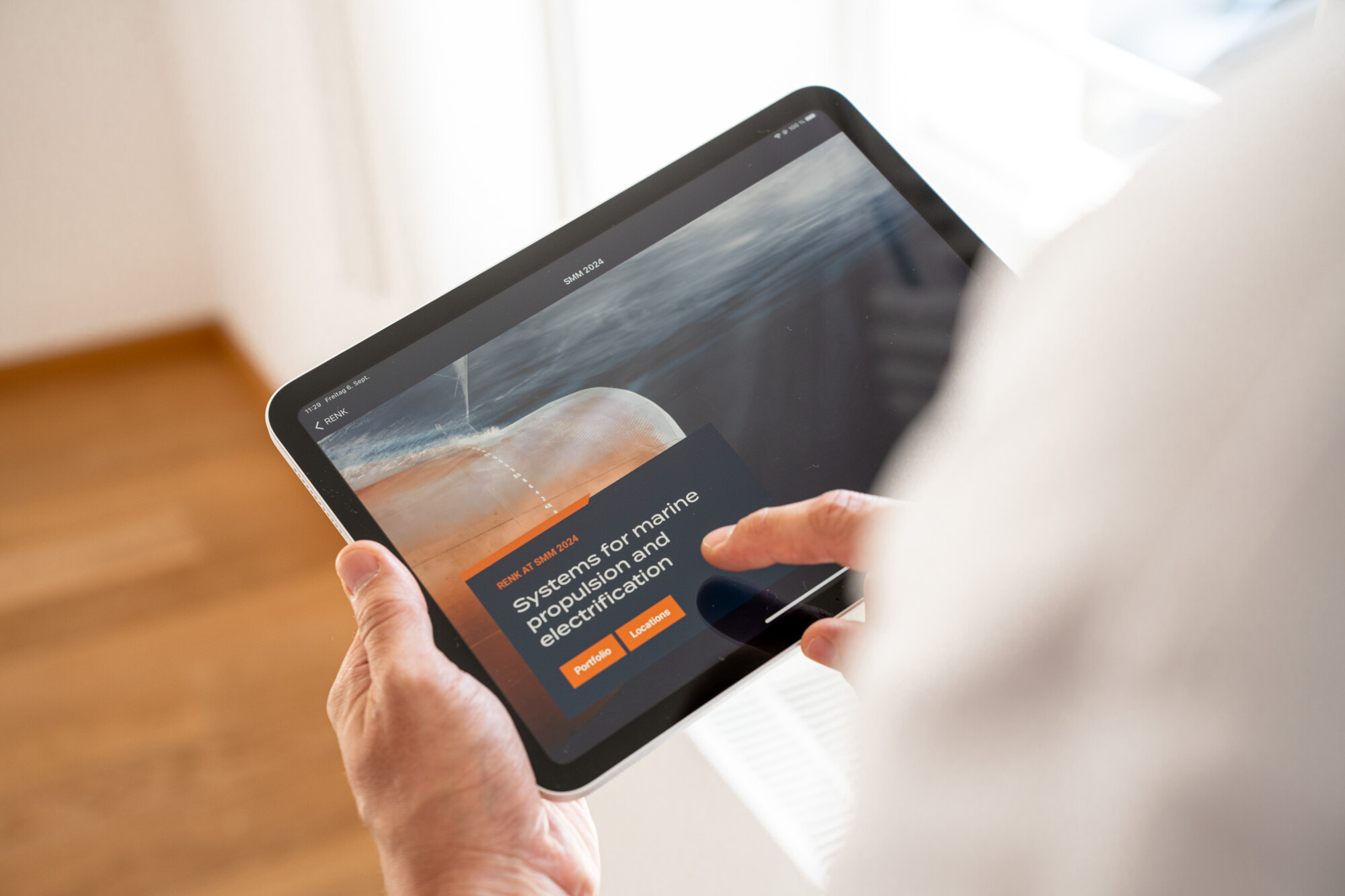Person hält Tablet mit Website zu Systemen für marine Antriebselektrifizierung, klickt auf Buttons „Product“ und „Solution“.