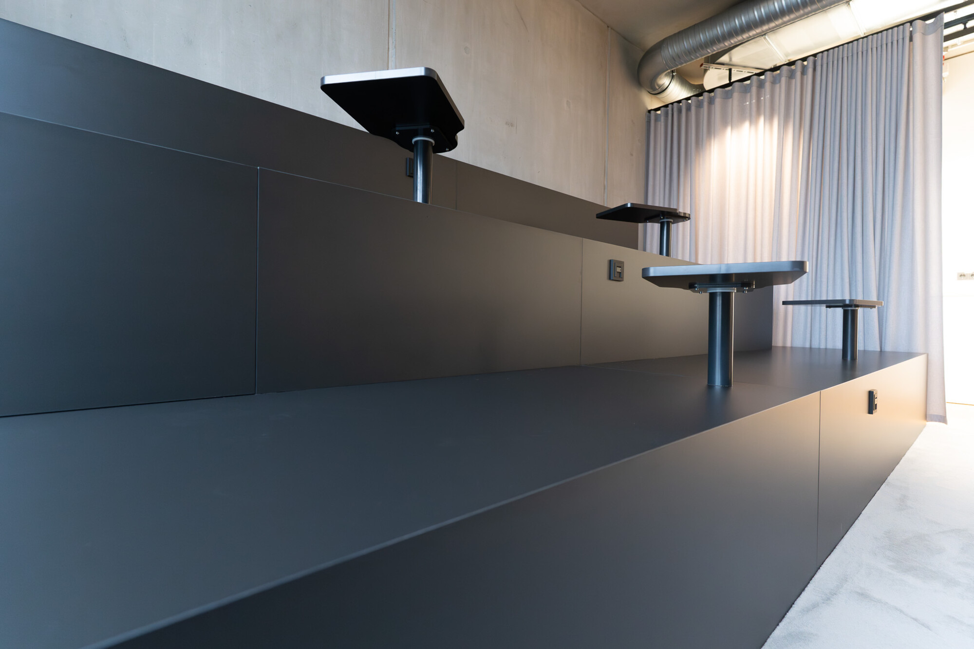 Moderne schwarze Sitzstufen mit aufgesetzten kleinen Tischen in heller, minimalistisch gestalteter Innenraumumgebung.