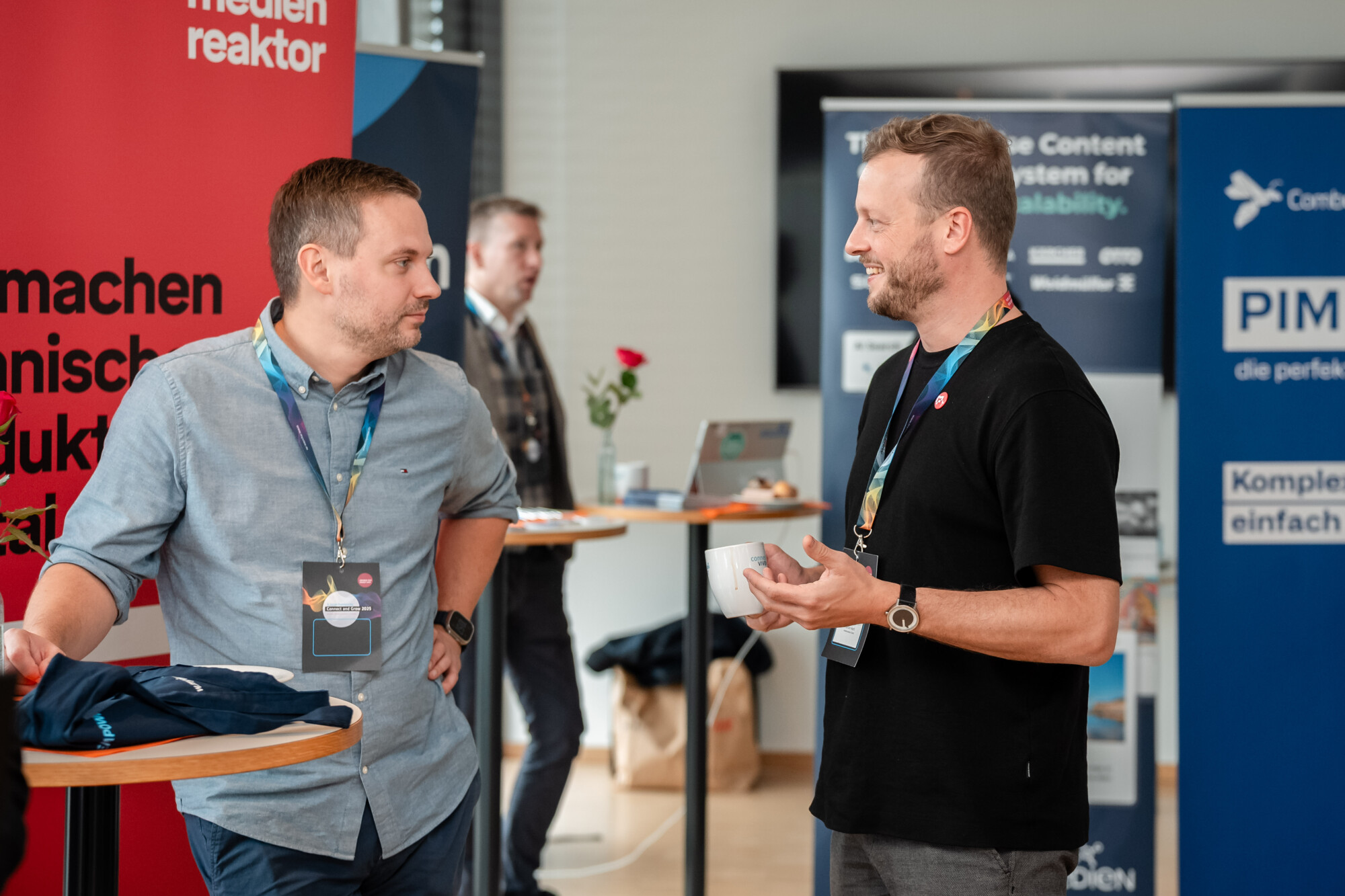 Zwei Männer im Gespräch auf einer Business-Veranstaltung mit medienreaktor-Messestand im Hintergrund.