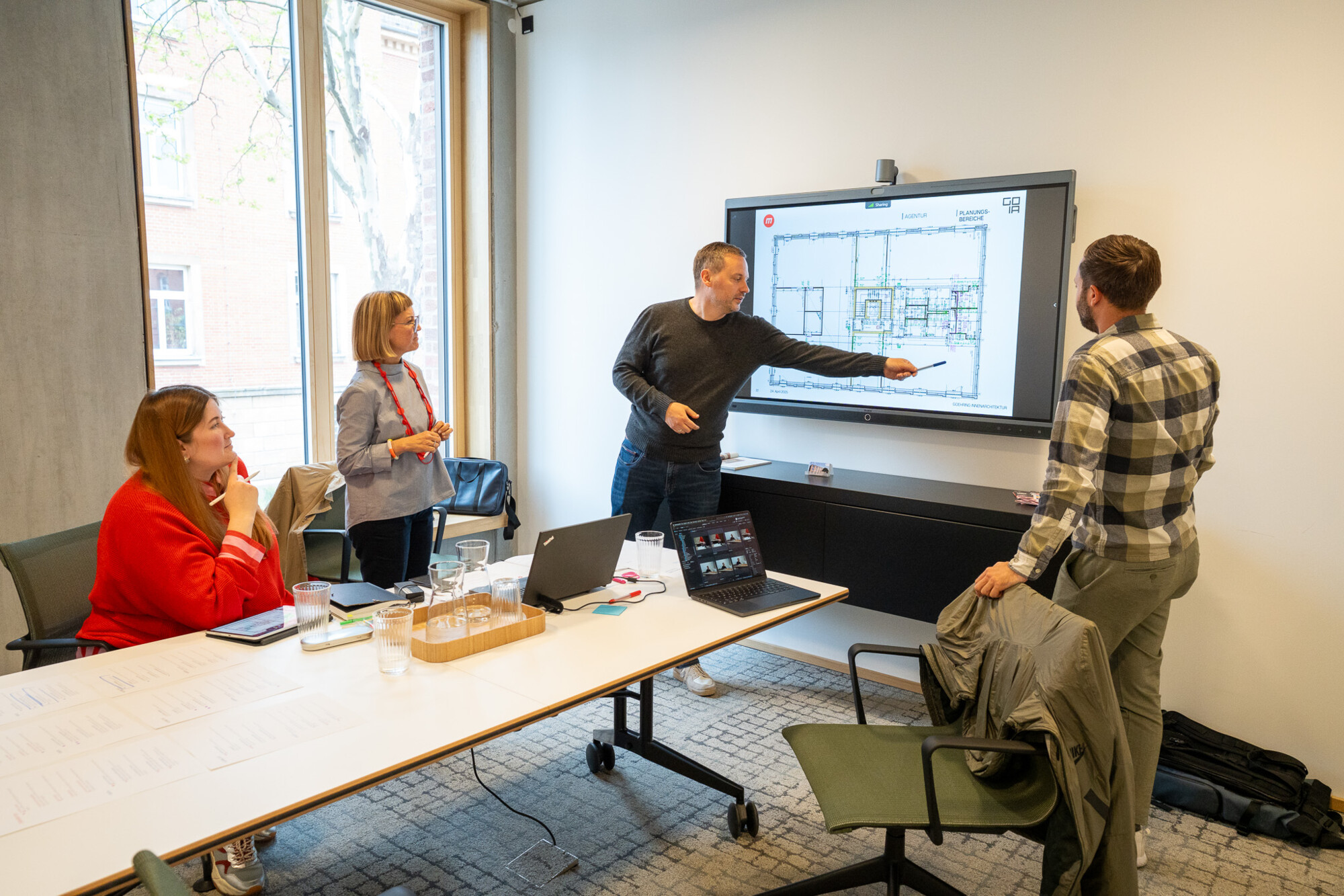 Team diskutiert Bauplan-Details auf großem Bildschirm in modernem Meetingraum bei Strategieplanung.